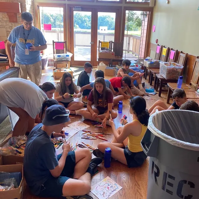 A group of volunteers seated on the floor assembling school supplies.