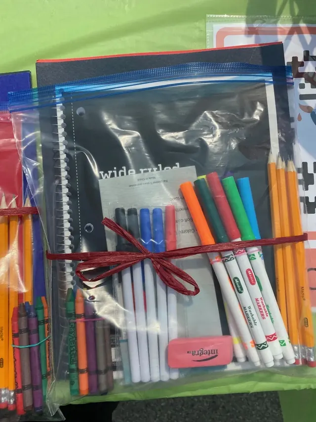 A clear bag packed with notebooks, colored pencils, pens, and other school supplies.
