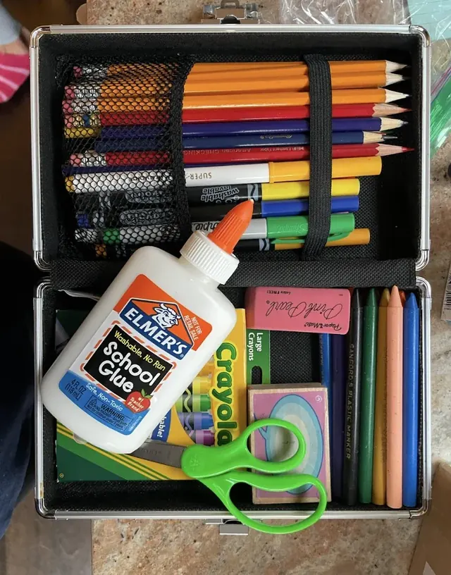 Pencils, scissors, glue, and colored craft supplies arranged in a storage box.