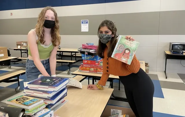 Two masked volunteers sorting donated books and materials at a table.