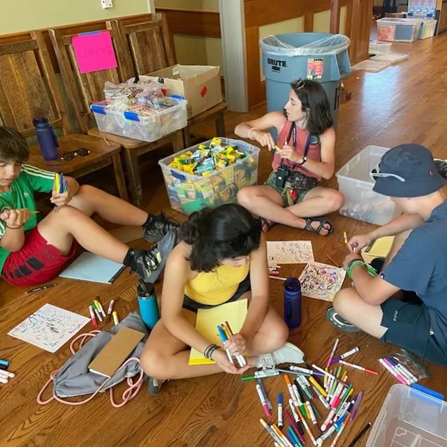 Volunteers seated on the floor sorting pencils, notebooks, and other donated materials.